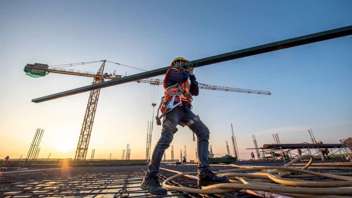 Bauarbeiter trägt Stahlträger auf Baustelle