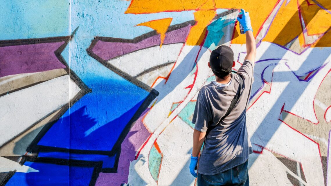 Street Art Künstler besprüht farbige Wand mit Graffiti